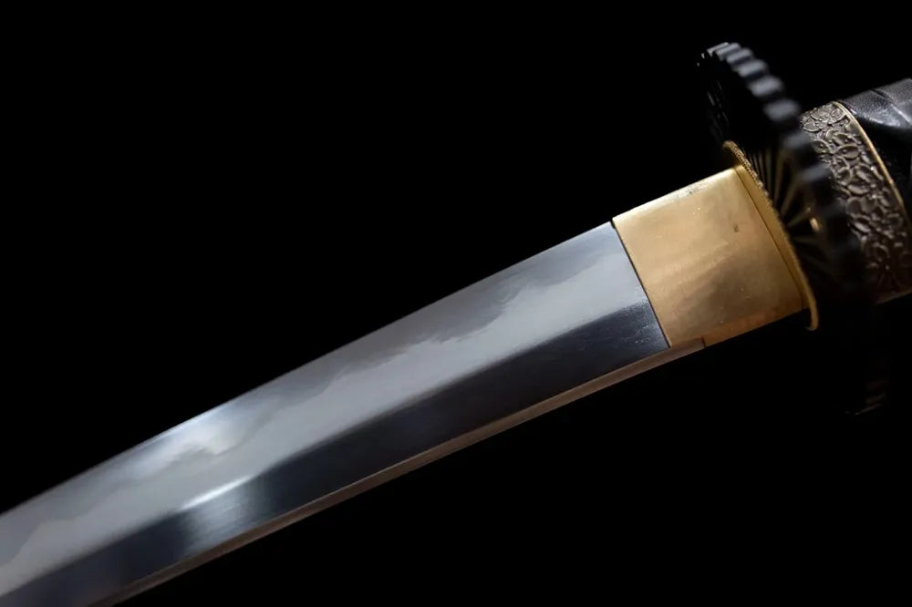 Upper T10 clay‑tempered tachi blade brass habaki midare irregular undulating hamon temper‑line macro close‑up