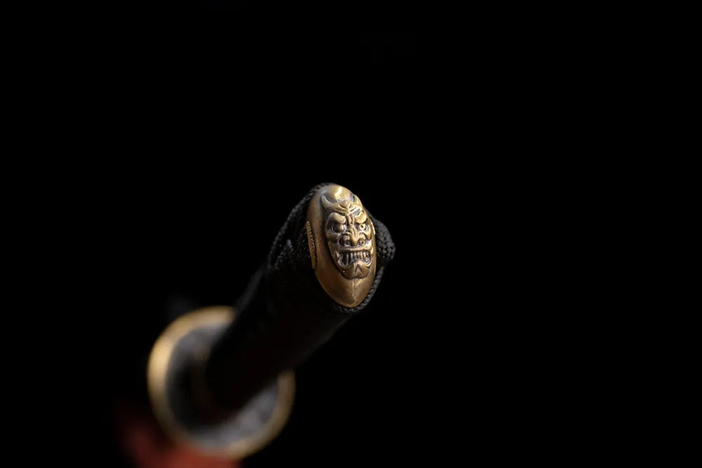 Carved demon‑mask brass pommel‑cap detail shot