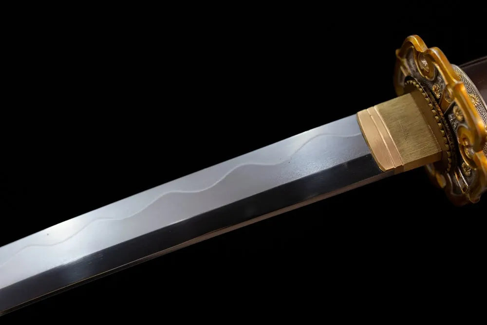 Upper T10 clay‑tempered tachi blade brass habaki gunome‑suguha layered‑chrysanthemum‑petal hamon temper‑line macro close‑up