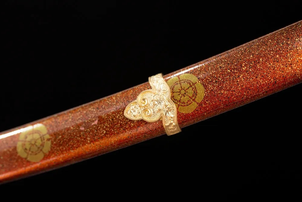 Mid‑section orange‑red lacquer hardwood tachi saya gold‑maki‑e sengoku‑clan‑kamon‑crest graphic texture close‑up